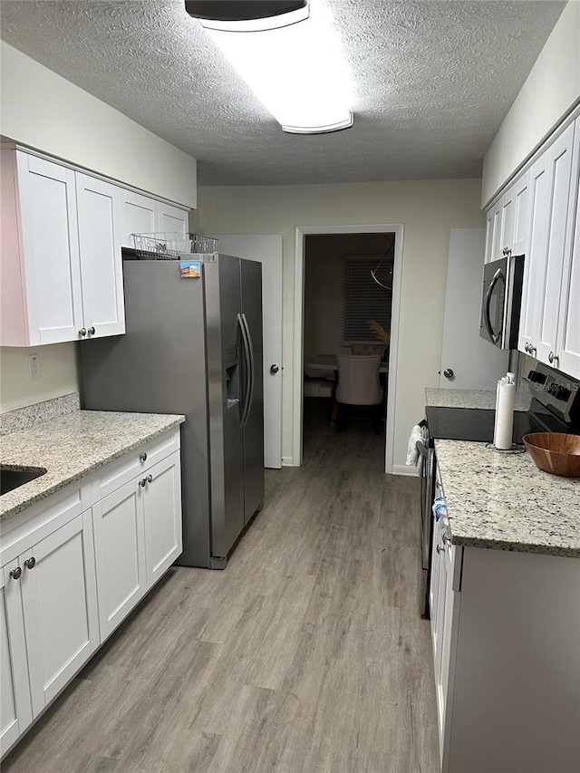 2902 Little Rd, Valrico, FL 33596 - kitchen with light wood-type flooring, appliances with stainless steel finishes, light stone counters, and a textured ceiling