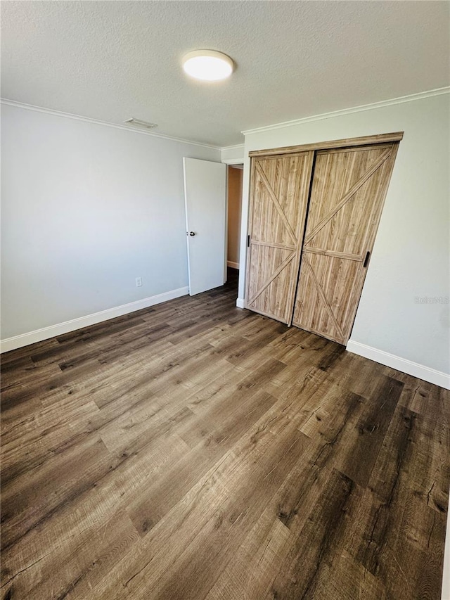 unfurnished bedroom featuring baseboards, ornamental molding, a textured ceiling, and wood finished floors