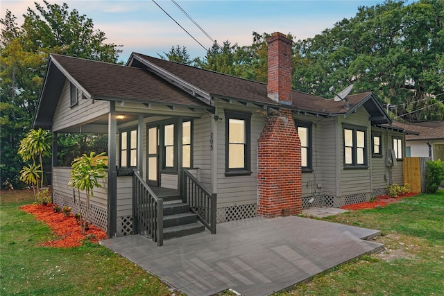view of front of property featuring a shingled roof, a front lawn, crawl space, a chimney, and a patio area