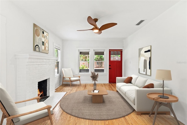 living room with a ceiling fan, visible vents, a fireplace, baseboards, and light wood finished floors