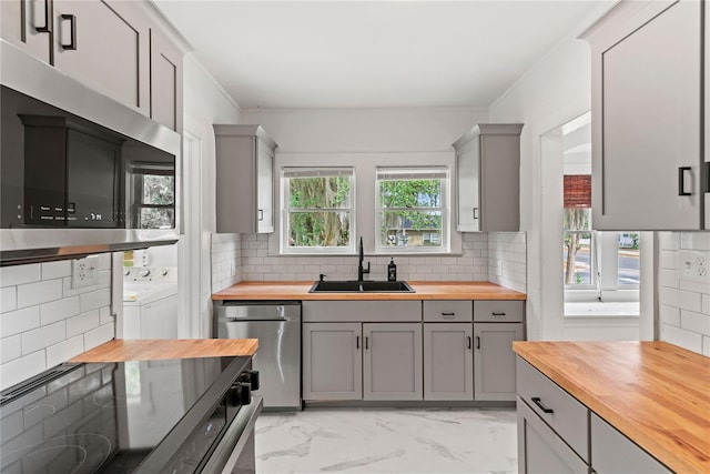 kitchen featuring appliances with stainless steel finishes, a sink, wooden counters, gray cabinetry, and washing machine and dryer