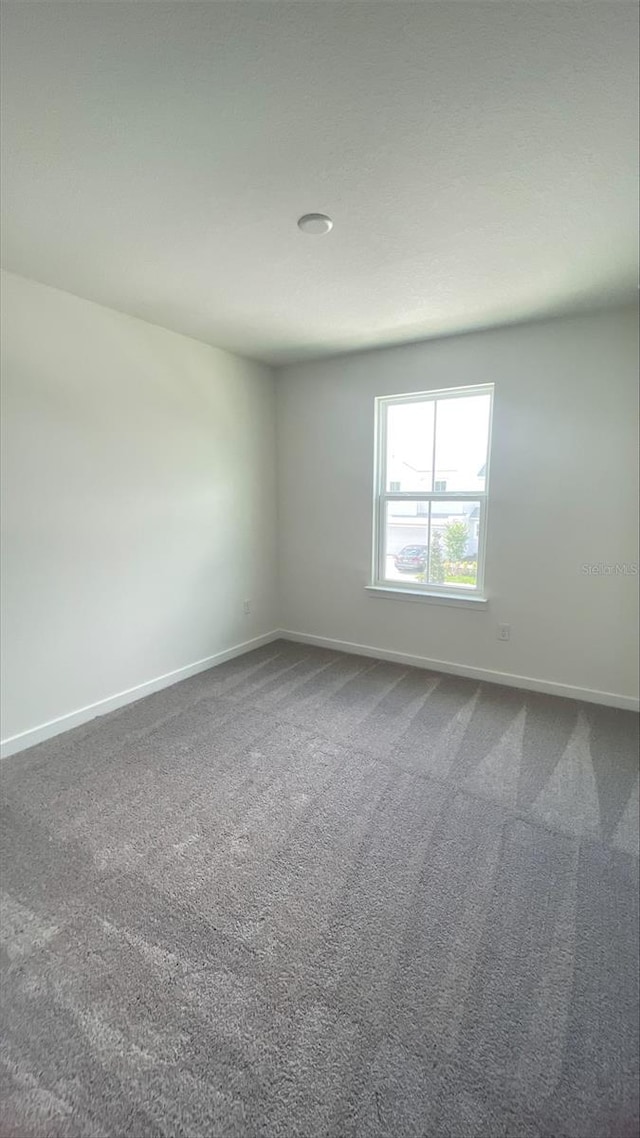 unfurnished room featuring dark colored carpet and baseboards