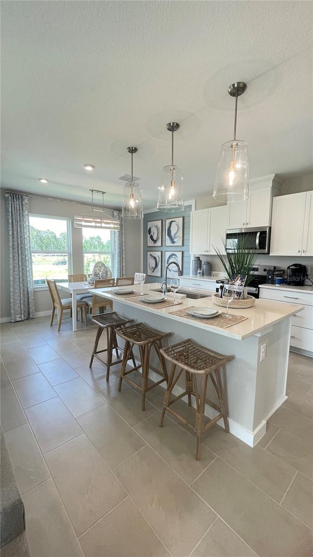 kitchen with white cabinets, a kitchen island with sink, light tile patterned floors, light countertops, and stainless steel microwave
