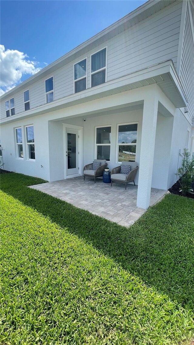 back of house featuring an outdoor living space, a patio area, a yard, and stucco siding
