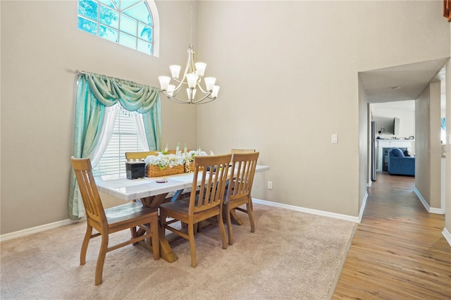 dining area featuring baseboards, light wood-type flooring, a notable chandelier, and a high ceiling