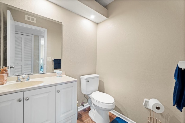 bathroom with visible vents, toilet, a textured wall, vanity, and wood finished floors