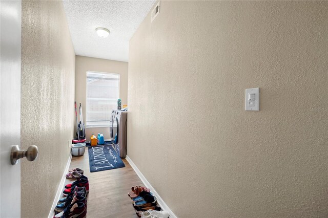 hall featuring visible vents, baseboards, washer and dryer, a textured ceiling, and wood finished floors