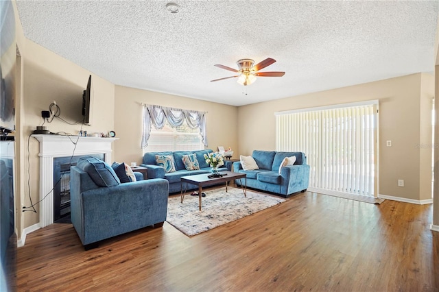 living area featuring baseboards, a fireplace, a textured ceiling, a ceiling fan, and wood finished floors