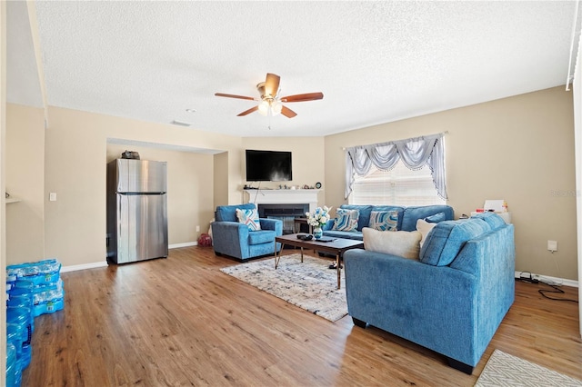 living room featuring a glass covered fireplace, baseboards, a textured ceiling, ceiling fan, and wood finished floors