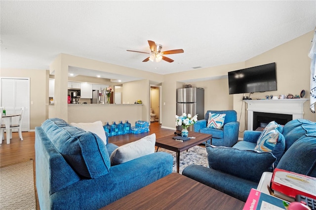 living room with a fireplace, light wood finished floors, baseboards, and ceiling fan
