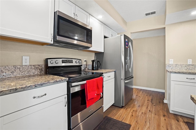 kitchen featuring baseboards, light wood-style flooring, white cabinets, visible vents, and stainless steel appliances