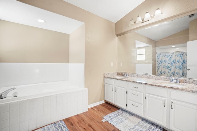 bathroom with a bath, wood finished floors, double vanity, and a sink