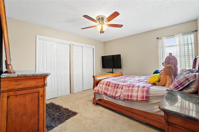 bedroom featuring ceiling fan, two closets, light carpet, and a textured ceiling
