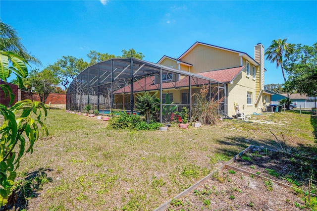 back of house with a chimney, a vegetable garden, a lawn, and a lanai