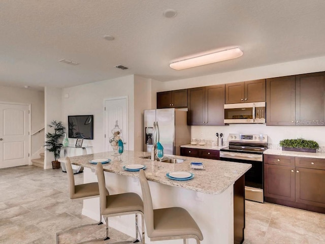 1550 Dalehurst Ln, Kissimmee, FL 34744 - kitchen with visible vents, a kitchen island with sink, a kitchen bar, light stone countertops, and stainless steel appliances