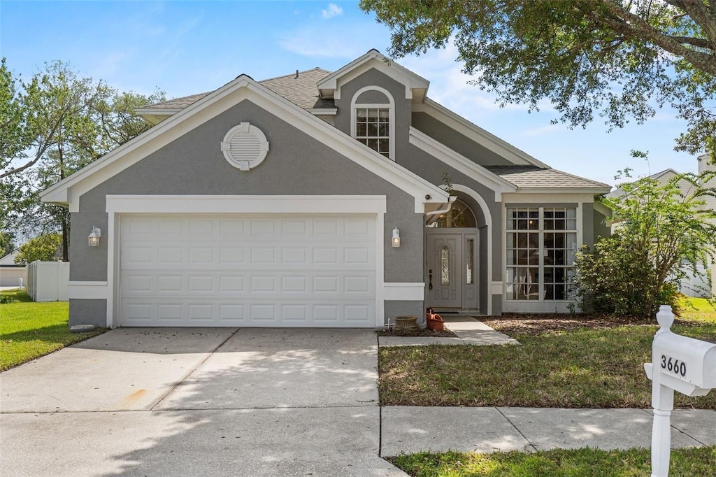 traditional-style house featuring a garage, stucco siding, a front yard, a shingled roof, and driveway