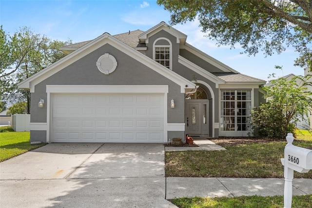 traditional-style house featuring a garage, stucco siding, a front yard, a shingled roof, and driveway