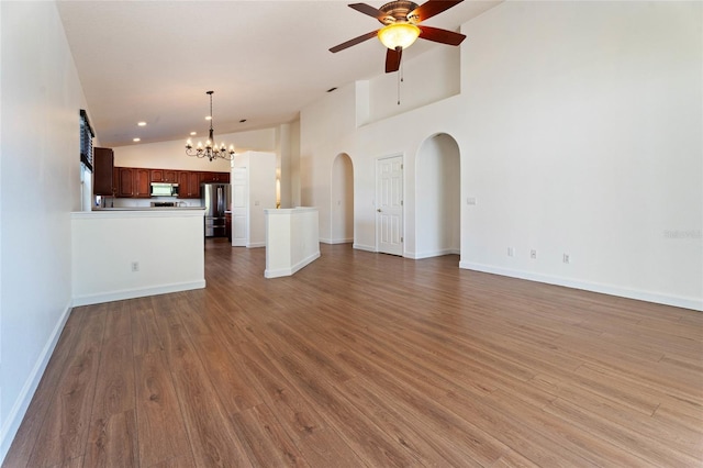 unfurnished living room with ceiling fan, arched walkways, vaulted ceiling, wood finished floors, and a chandelier