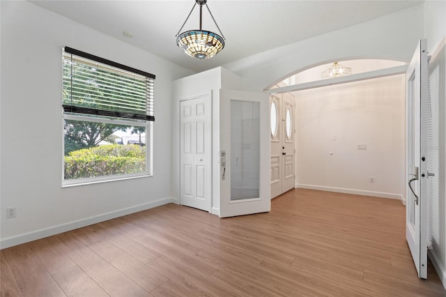 unfurnished bedroom featuring a chandelier, multiple windows, light wood-style flooring, and baseboards