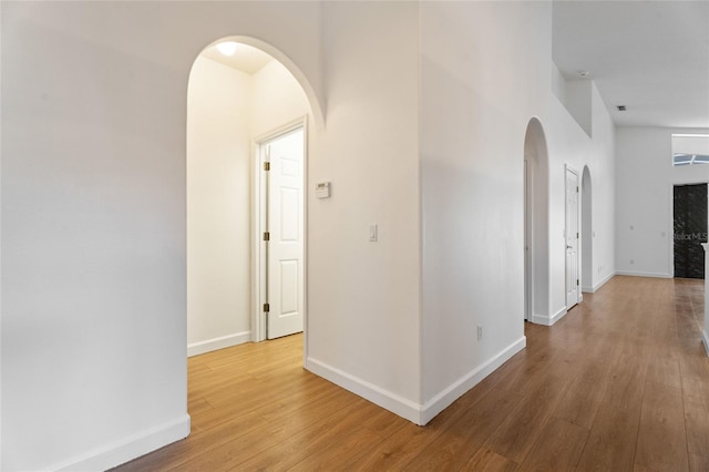 hallway with wood finished floors, arched walkways, and baseboards
