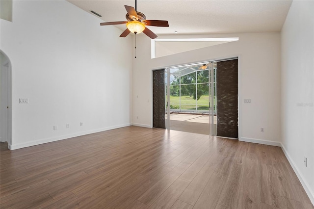spare room featuring ceiling fan, arched walkways, wood finished floors, baseboards, and high vaulted ceiling