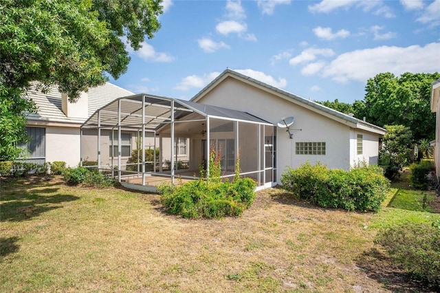 rear view of house featuring a yard, glass enclosure, and stucco siding