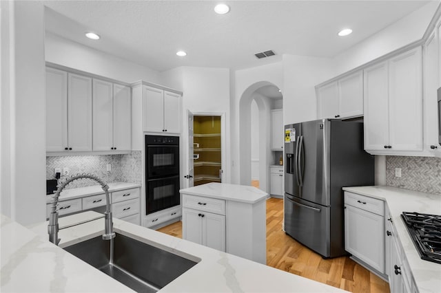 1803 Glenbay Ct, Windermere, FL 34786 - kitchen featuring arched walkways, light stone counters, a sink, backsplash, and black appliances