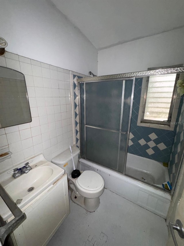 bathroom featuring toilet, vanity, combined bath / shower with glass door, and tile walls