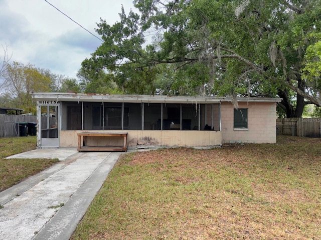 view of front of house featuring concrete block siding, a front lawn, fence, and a sunroom