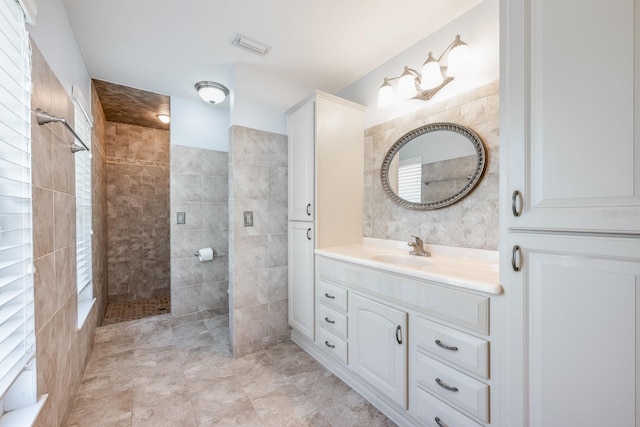 bathroom with tile walls, walk in shower, vanity, and visible vents