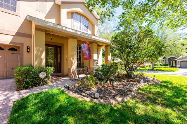 doorway to property featuring a garage, stucco siding, and a lawn