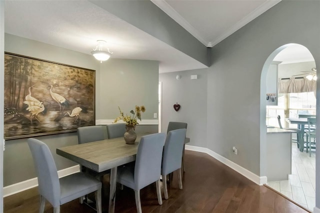 dining area featuring arched walkways, wood finished floors, crown molding, and baseboards