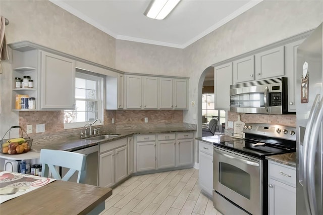 kitchen with tasteful backsplash, crown molding, stainless steel appliances, arched walkways, and a sink