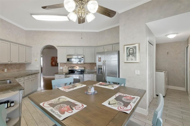 dining room with washer / clothes dryer, baseboards, arched walkways, ornamental molding, and a ceiling fan