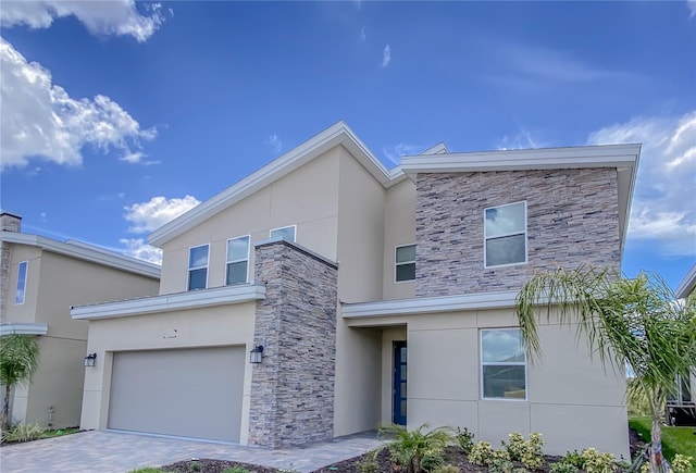 contemporary house featuring stucco siding, stone siding, decorative driveway, and an attached garage