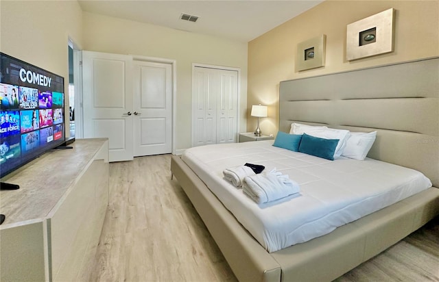 bedroom featuring light wood finished floors, visible vents, and multiple closets