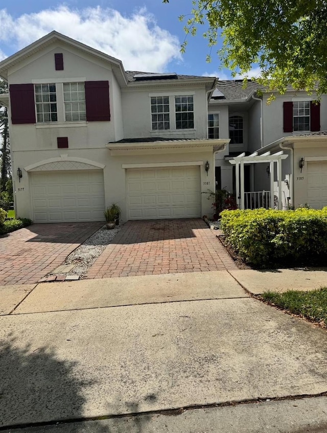 view of front of home with decorative driveway, an attached garage, roof mounted solar panels, and stucco siding
