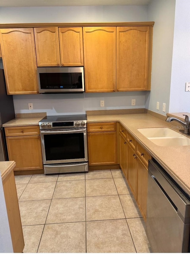 kitchen featuring brown cabinetry, light countertops, a sink, light tile patterned floors, and stainless steel appliances