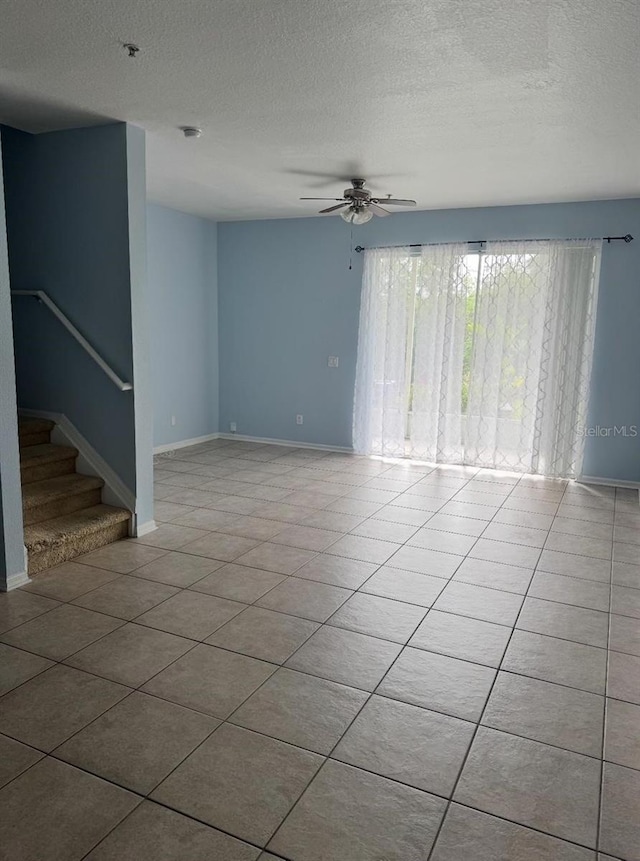 unfurnished living room featuring a textured ceiling, ceiling fan, stairway, and tile patterned flooring