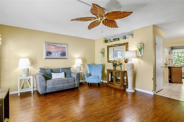 living area with a textured ceiling, baseboards, wood finished floors, and ceiling fan