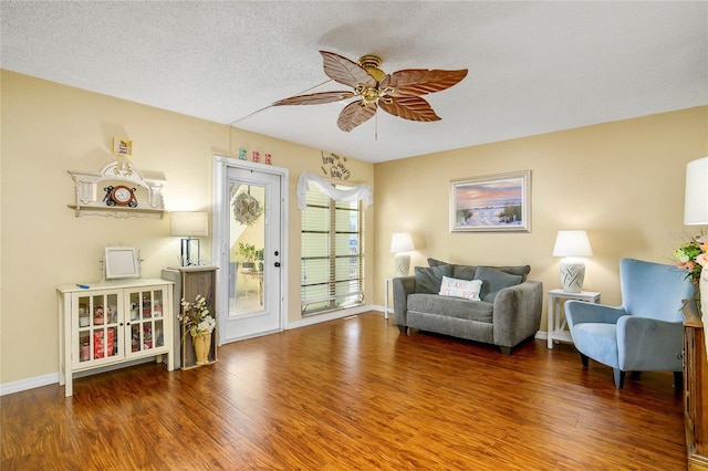 living area featuring a textured ceiling, wood finished floors, baseboards, and a ceiling fan