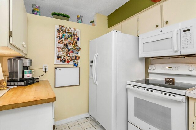 kitchen featuring light tile patterned floors, baseboards, wooden counters, white appliances, and white cabinetry