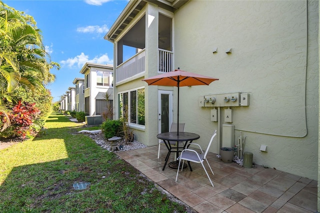 back of property featuring a patio, a balcony, stucco siding, and a lawn