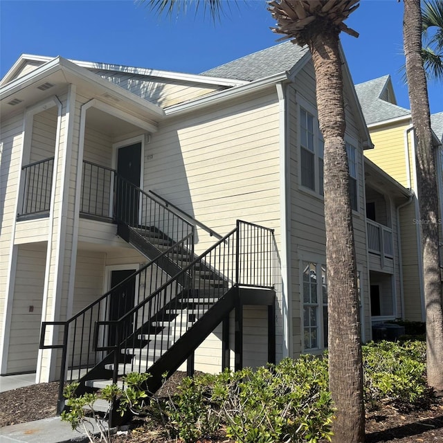 view of property exterior with a shingled roof and stairway