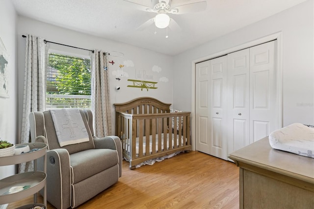bedroom with light wood finished floors, a crib, a closet, and ceiling fan