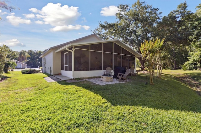 rear view of property featuring a lawn, an outdoor fire pit, a sunroom, and stucco siding