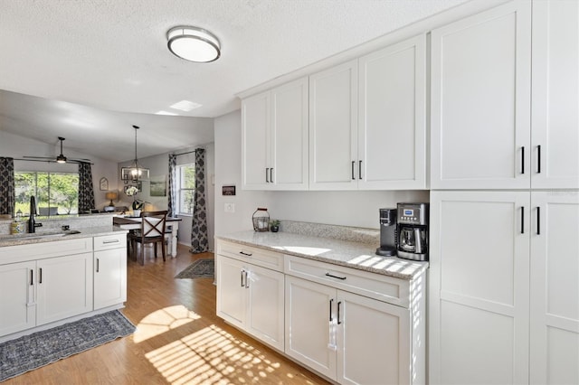 kitchen featuring white cabinets, a sink, light wood-style floors, light stone counters, and decorative light fixtures