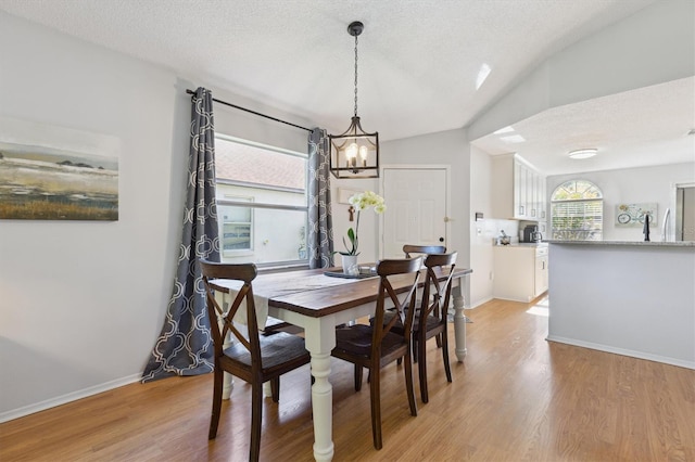 dining space featuring baseboards, a notable chandelier, a textured ceiling, and light wood-style flooring