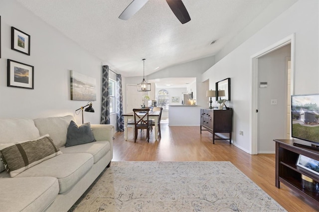 living area featuring a textured ceiling, visible vents, lofted ceiling, a ceiling fan, and wood finished floors