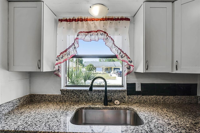 kitchen with a sink, decorative backsplash, dark stone counters, and white cabinets